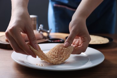 Making schnitzel. Woman coating slice of meat with bread crumbs at wooden table, closeup