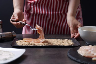 Making schnitzel. Woman coating slice of meat with bread crumbs at dark table, closeup