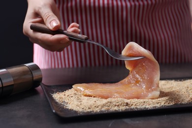 Making schnitzel. Woman coating slice of meat with bread crumbs at dark table, closeup