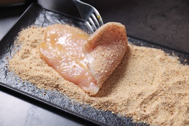 Photo of Making schnitzel. Coating slice of meat with bread crumbs at dark table, closeup