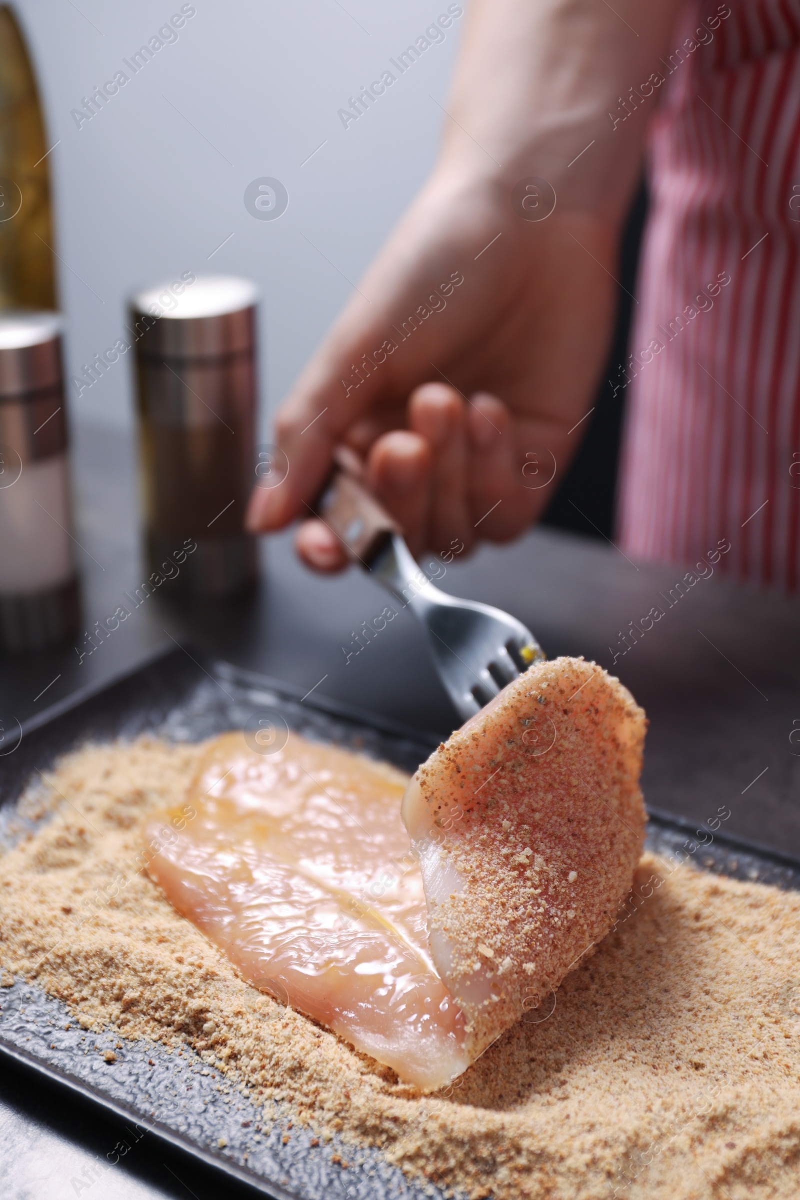 Photo of Making schnitzel. Woman coating slice of meat with bread crumbs at dark table, closeup