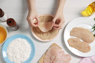 Photo of Making schnitzel. Woman coating slice of meat with bread crumbs at white wooden table, top view