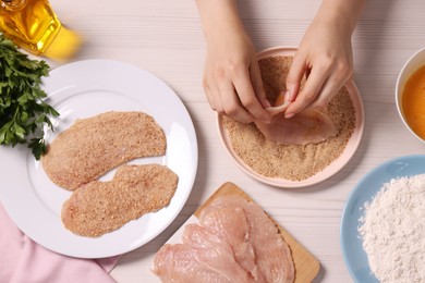 Photo of Making schnitzel. Woman coating slice of meat with bread crumbs at white wooden table, top view