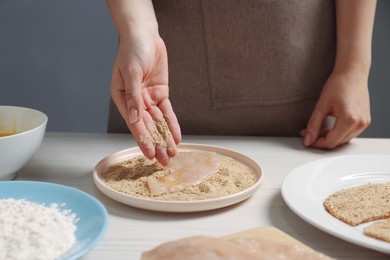 Photo of Making schnitzel. Woman coating slice of meat with bread crumbs at white wooden table, closeup