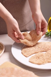 Photo of Making schnitzel. Woman putting slice of meat with bread crumbs onto plate at white wooden table, closeup