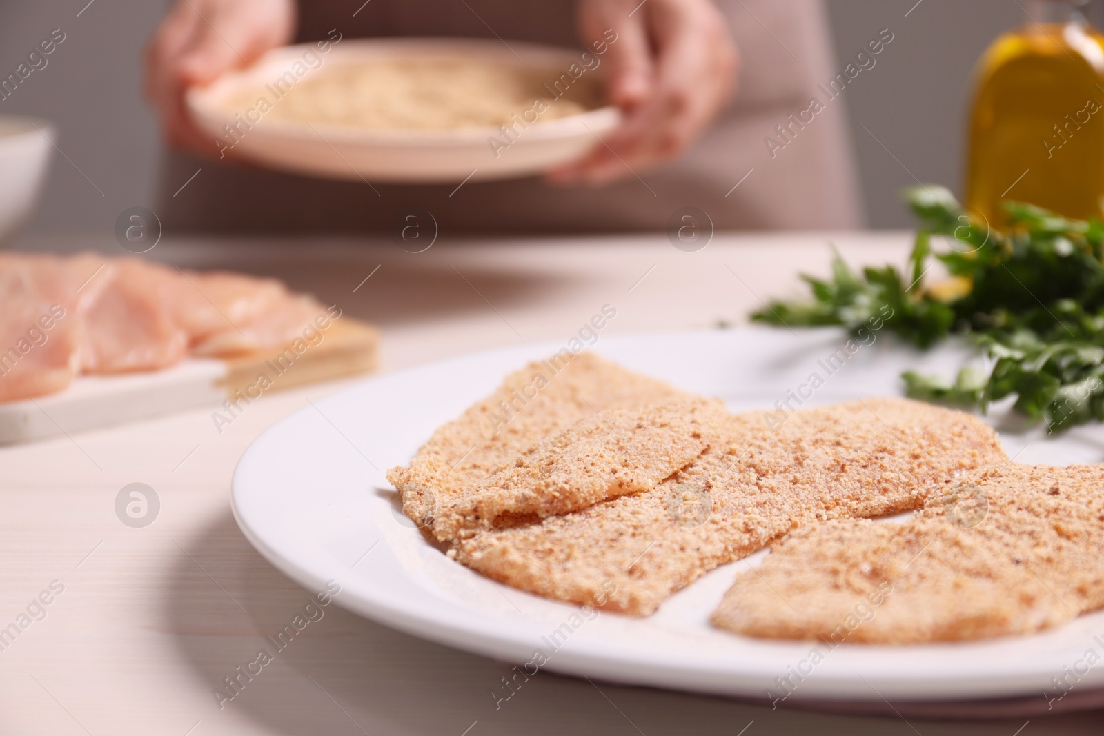 Photo of Woman making schnitzel at light wooden table, focus on slices of meat with bread crumbs