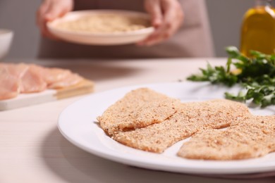 Woman making schnitzel at light wooden table, focus on slices of meat with bread crumbs