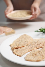 Woman making schnitzel at light wooden table, focus on slices of meat with bread crumbs