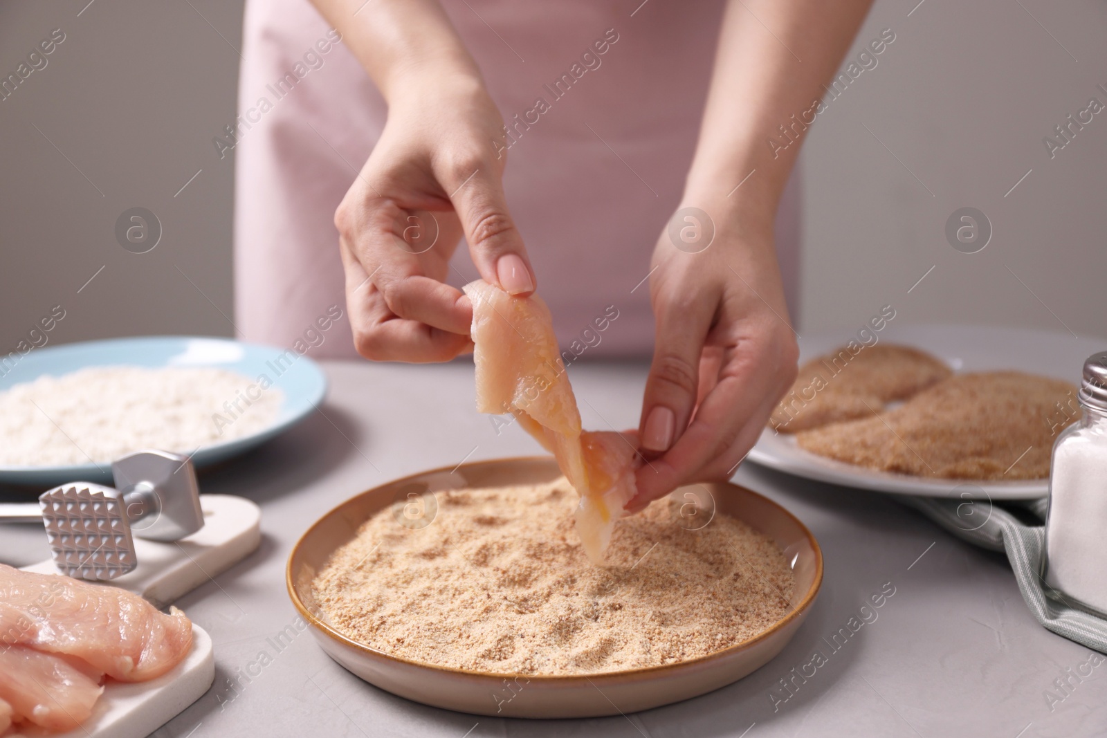 Photo of Making schnitzel. Woman coating slice of meat with bread crumbs at grey table, closeup