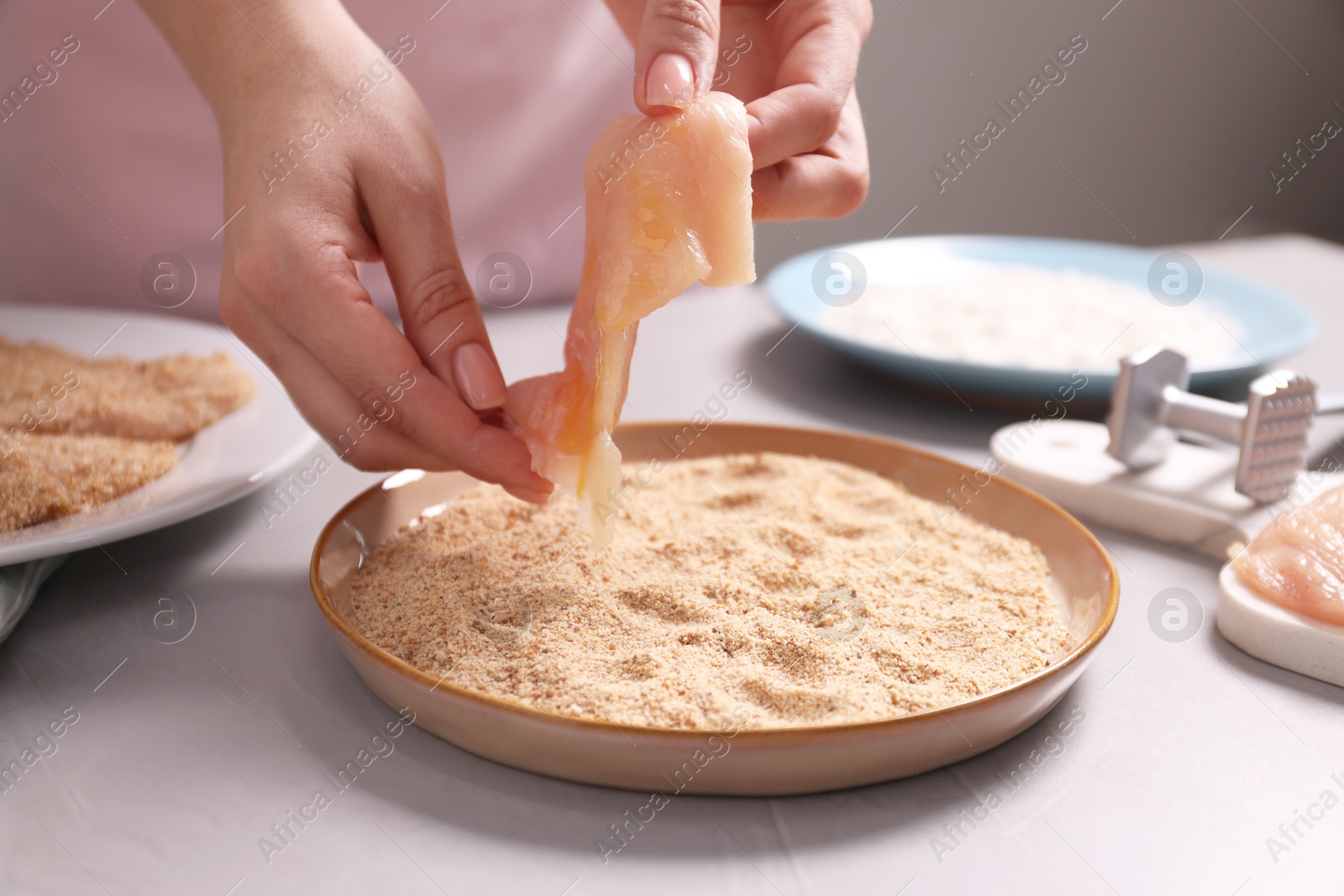 Photo of Making schnitzel. Woman coating slice of meat with bread crumbs at grey table, closeup