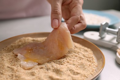 Making schnitzel. Woman coating slice of meat with bread crumbs at grey table, closeup