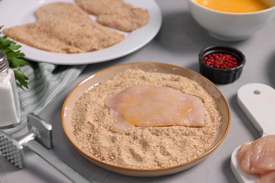 Photo of Making schnitzel. Plate with raw slice of meat in bread crumbs and tenderizer on grey table, closeup