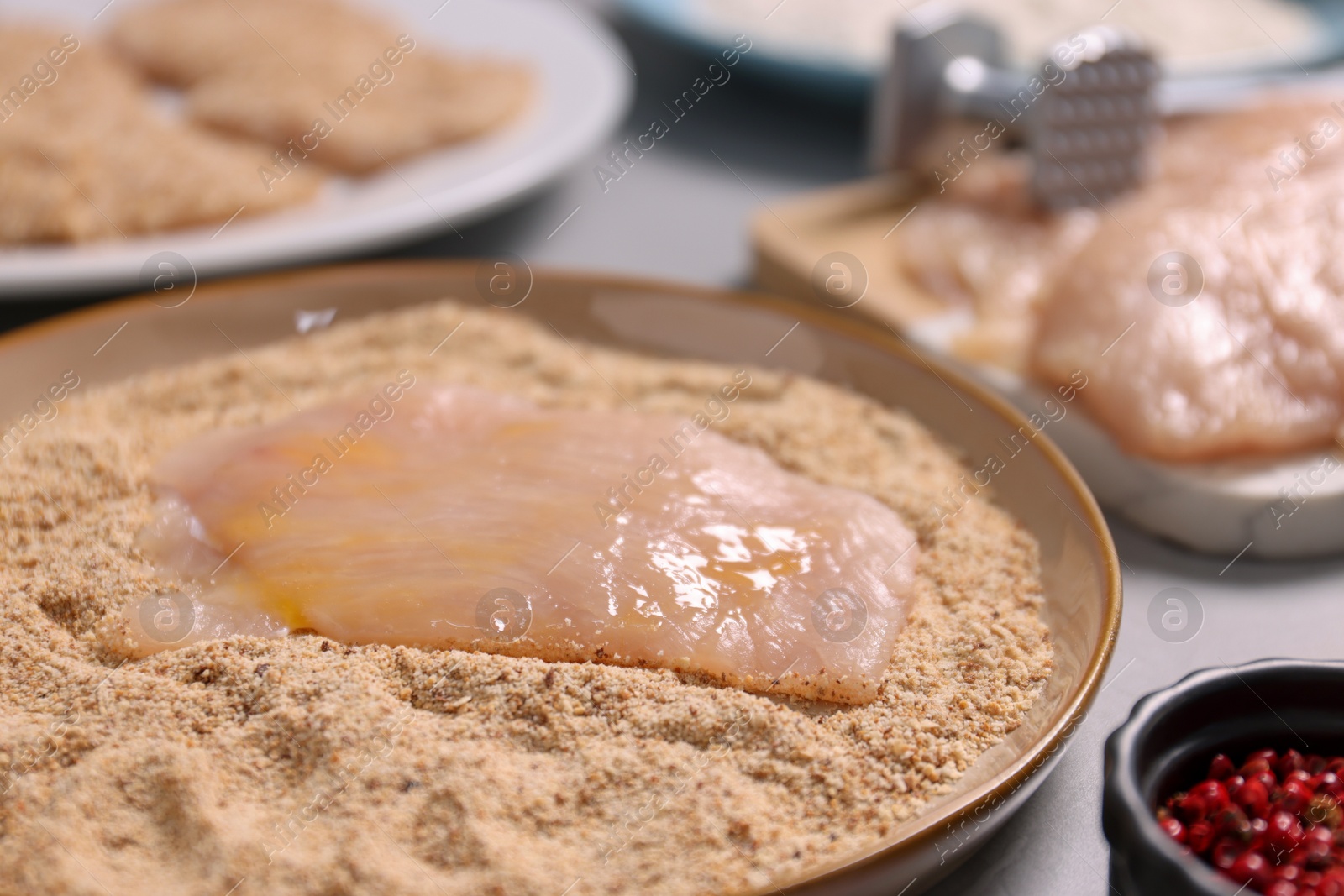 Photo of Making schnitzel. Plate with raw slice of meat in bread crumbs on grey table, closeup