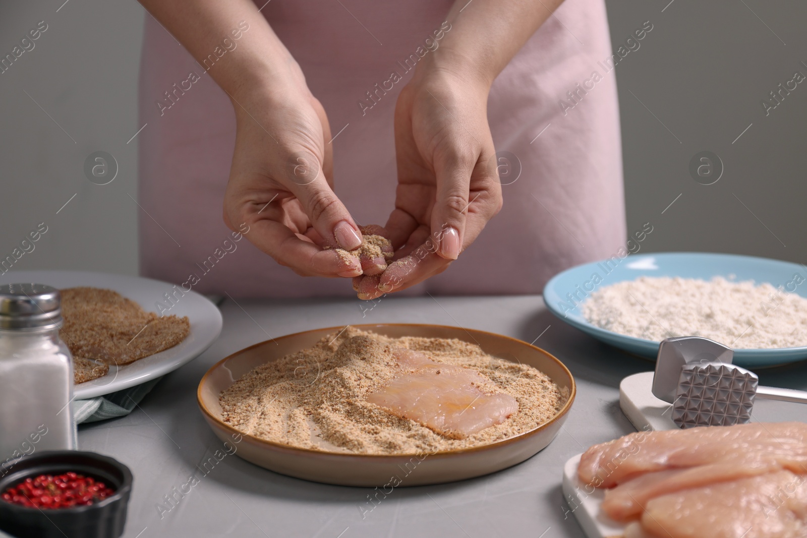 Photo of Making schnitzel. Woman coating slice of meat with bread crumbs at grey table, closeup