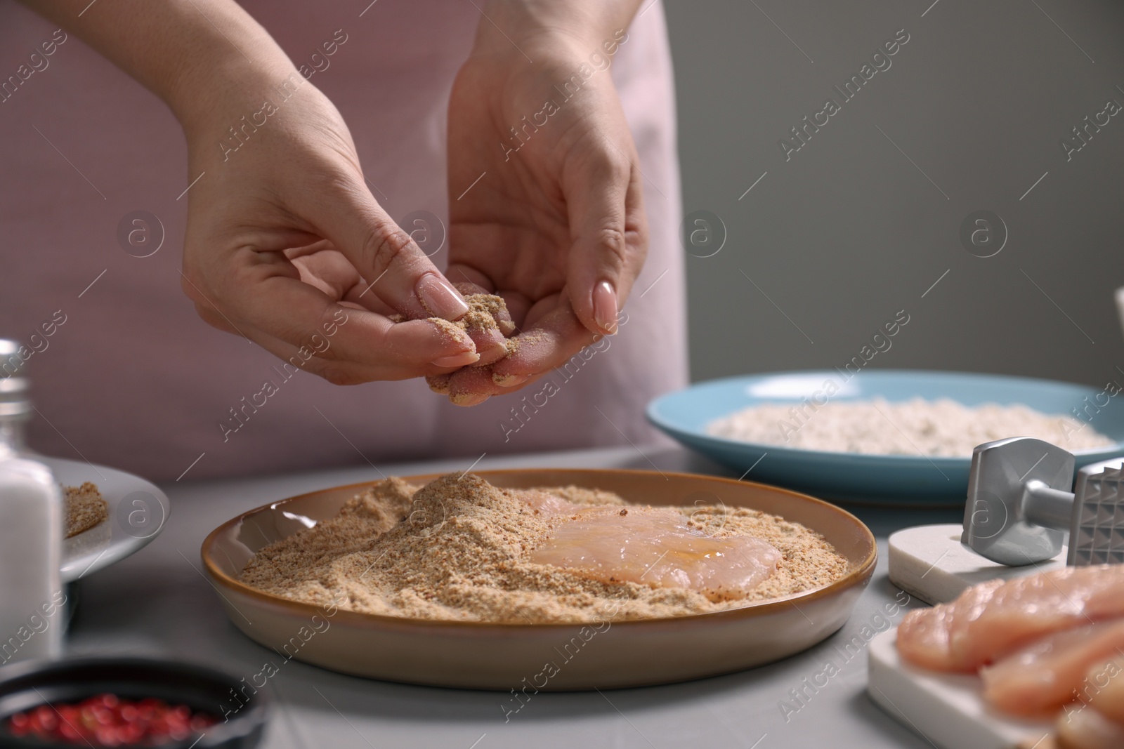 Photo of Making schnitzel. Woman coating slice of meat with bread crumbs at grey table, closeup