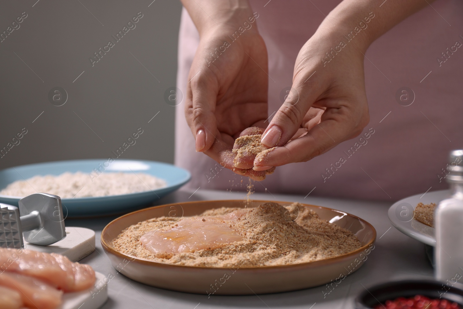 Photo of Making schnitzel. Woman coating slice of meat with bread crumbs at grey table, closeup