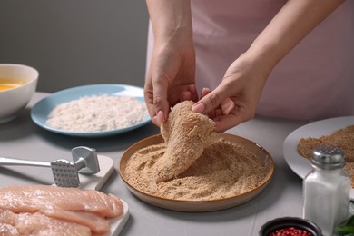 Photo of Making schnitzel. Woman coating slice of meat with bread crumbs at grey table, closeup