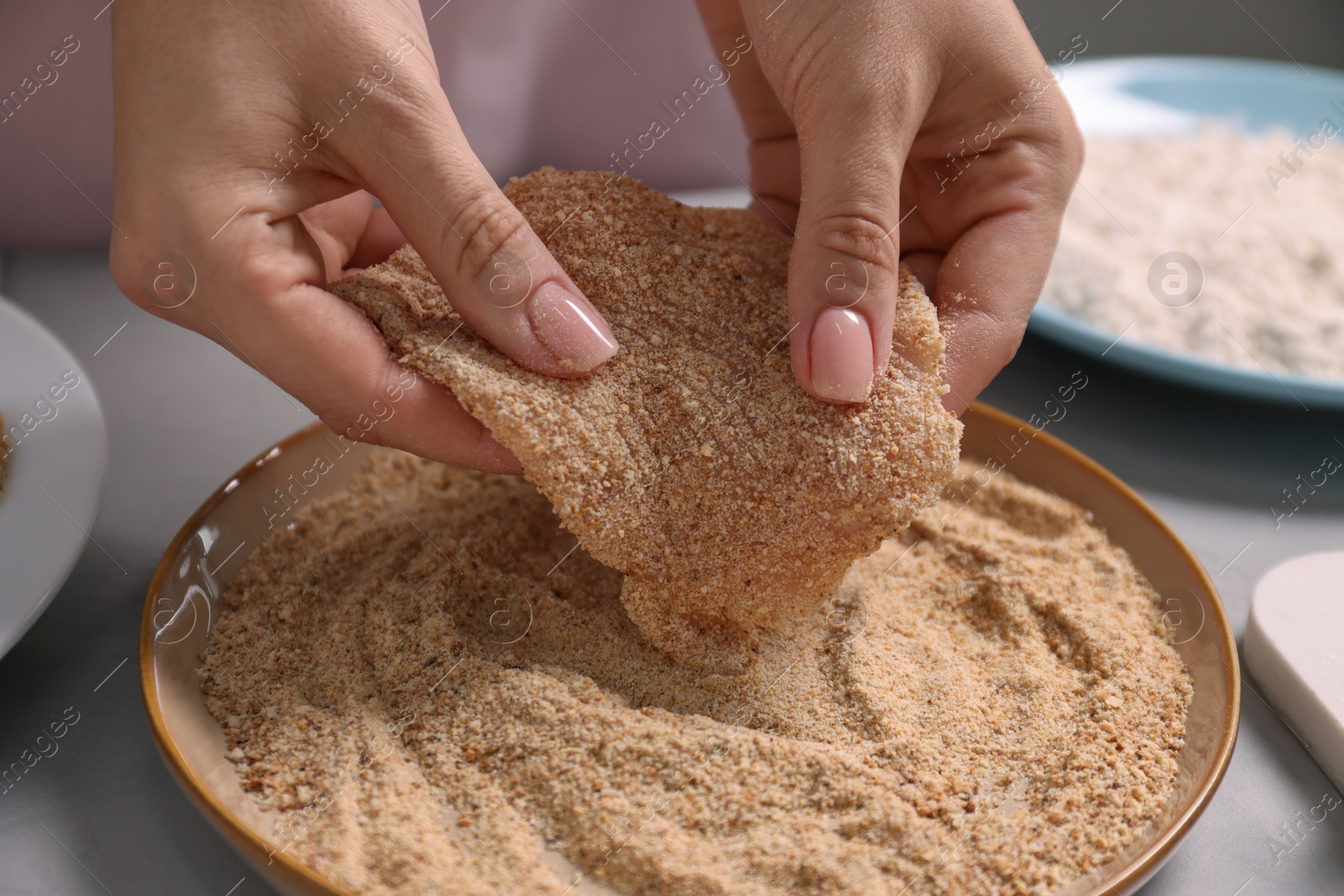 Photo of Making schnitzel. Woman coating slice of meat with bread crumbs at grey table, closeup