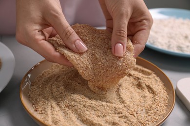 Making schnitzel. Woman coating slice of meat with bread crumbs at grey table, closeup