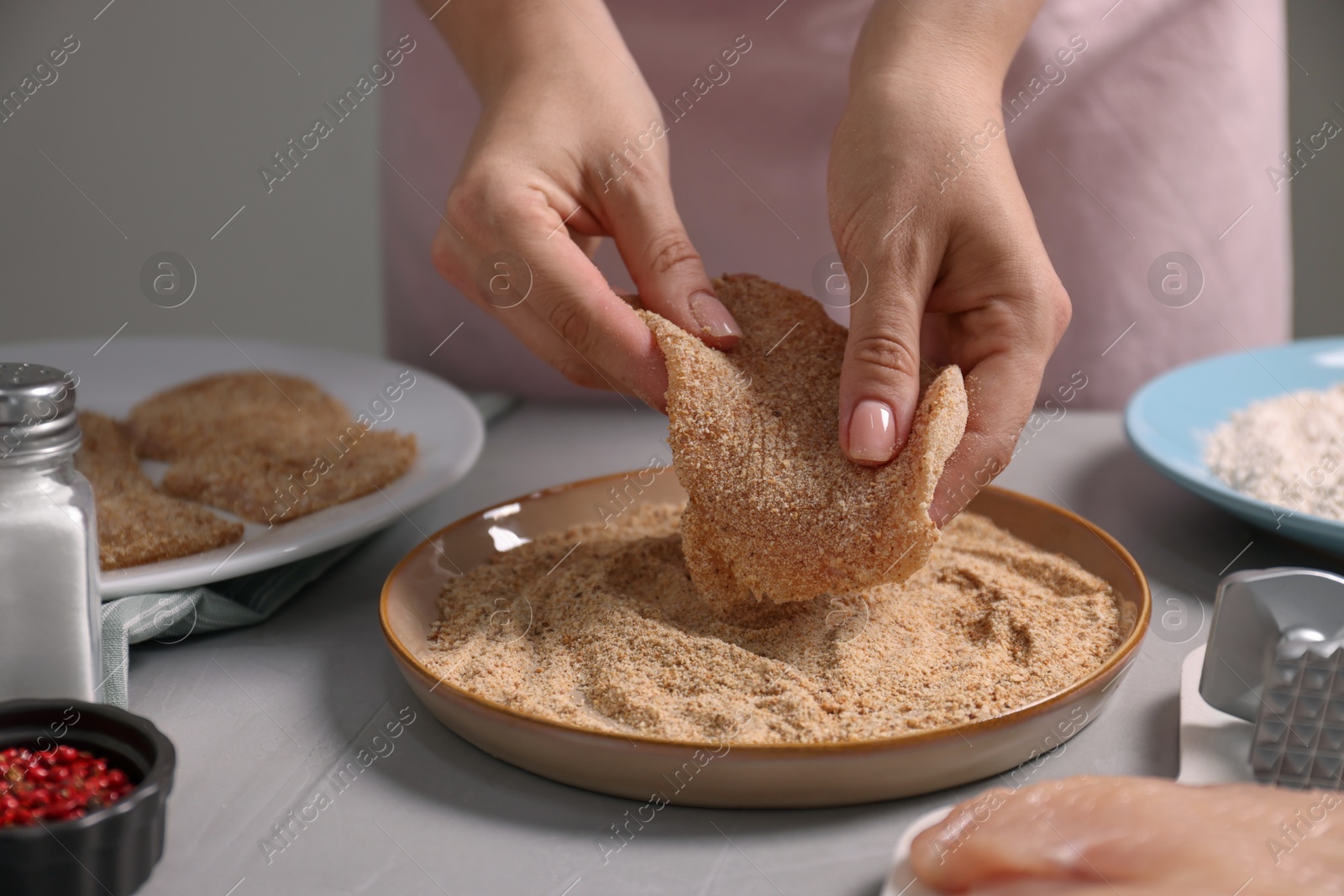 Photo of Making schnitzel. Woman coating slice of meat with bread crumbs at grey table, closeup