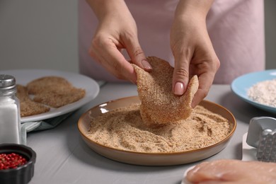 Making schnitzel. Woman coating slice of meat with bread crumbs at grey table, closeup