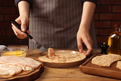 Photo of Woman making schnitzel at wooden table, closeup