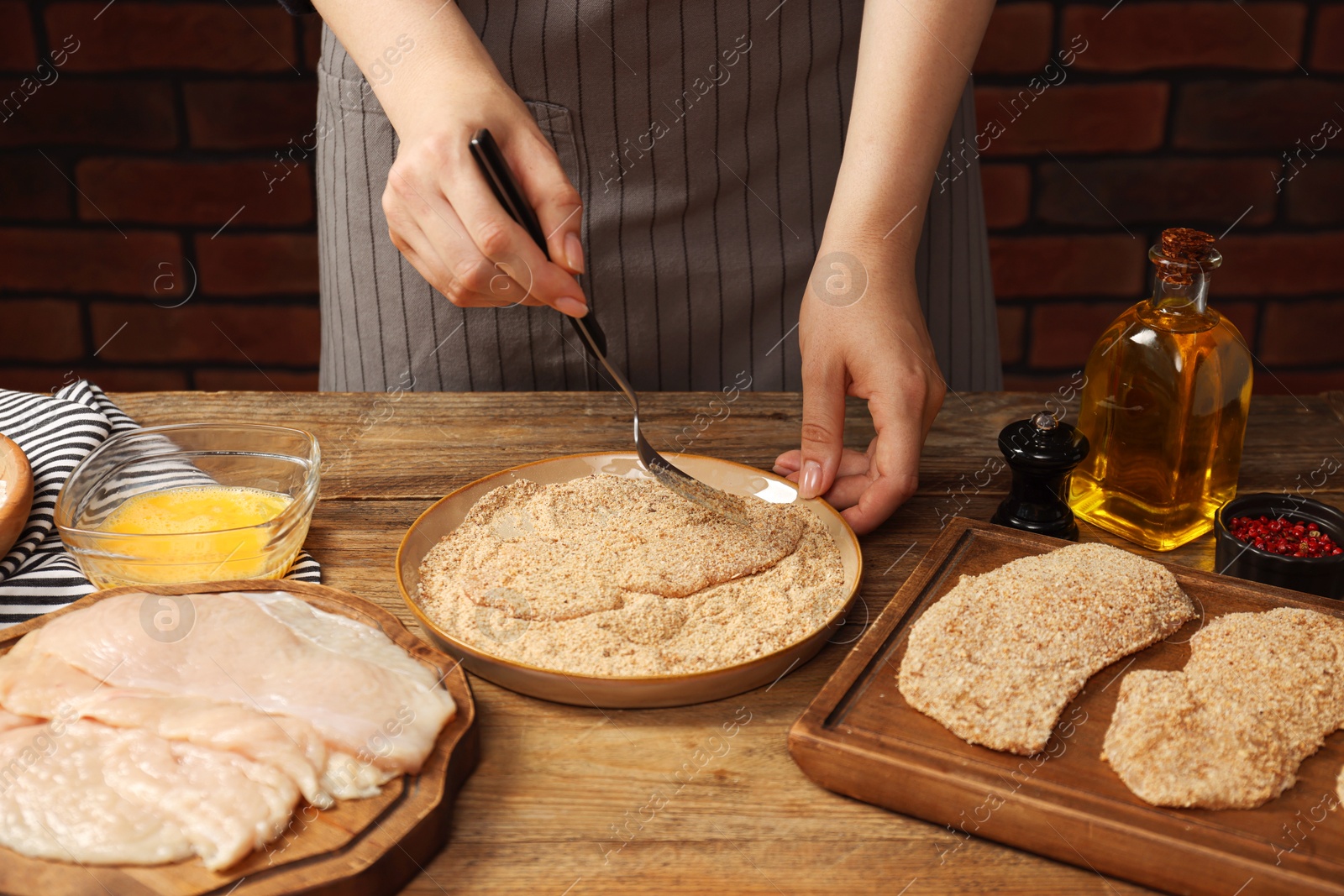 Photo of Woman making schnitzel at wooden table, closeup