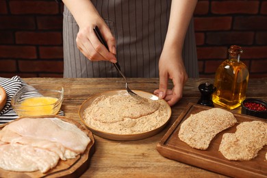 Woman making schnitzel at wooden table, closeup