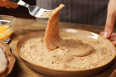 Photo of Woman making schnitzel at wooden table, closeup