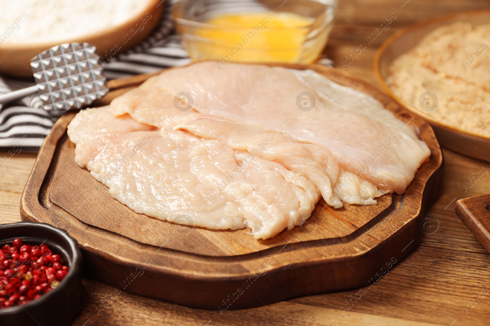 Photo of Making schnitzels. Raw meat and other ingredients on wooden table, closeup