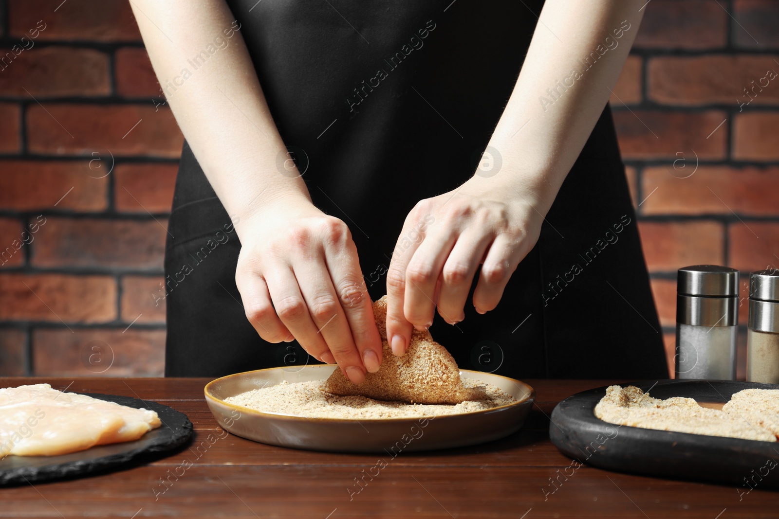 Photo of Woman making schnitzel at wooden table, closeup