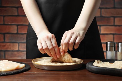 Woman making schnitzel at wooden table, closeup