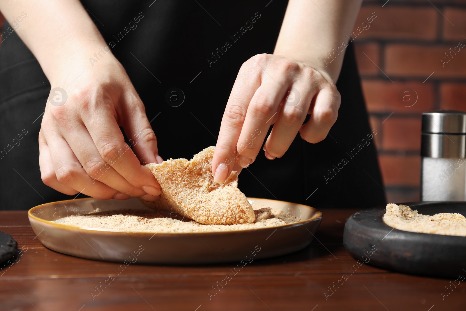 Photo of Woman making schnitzel at wooden table, closeup