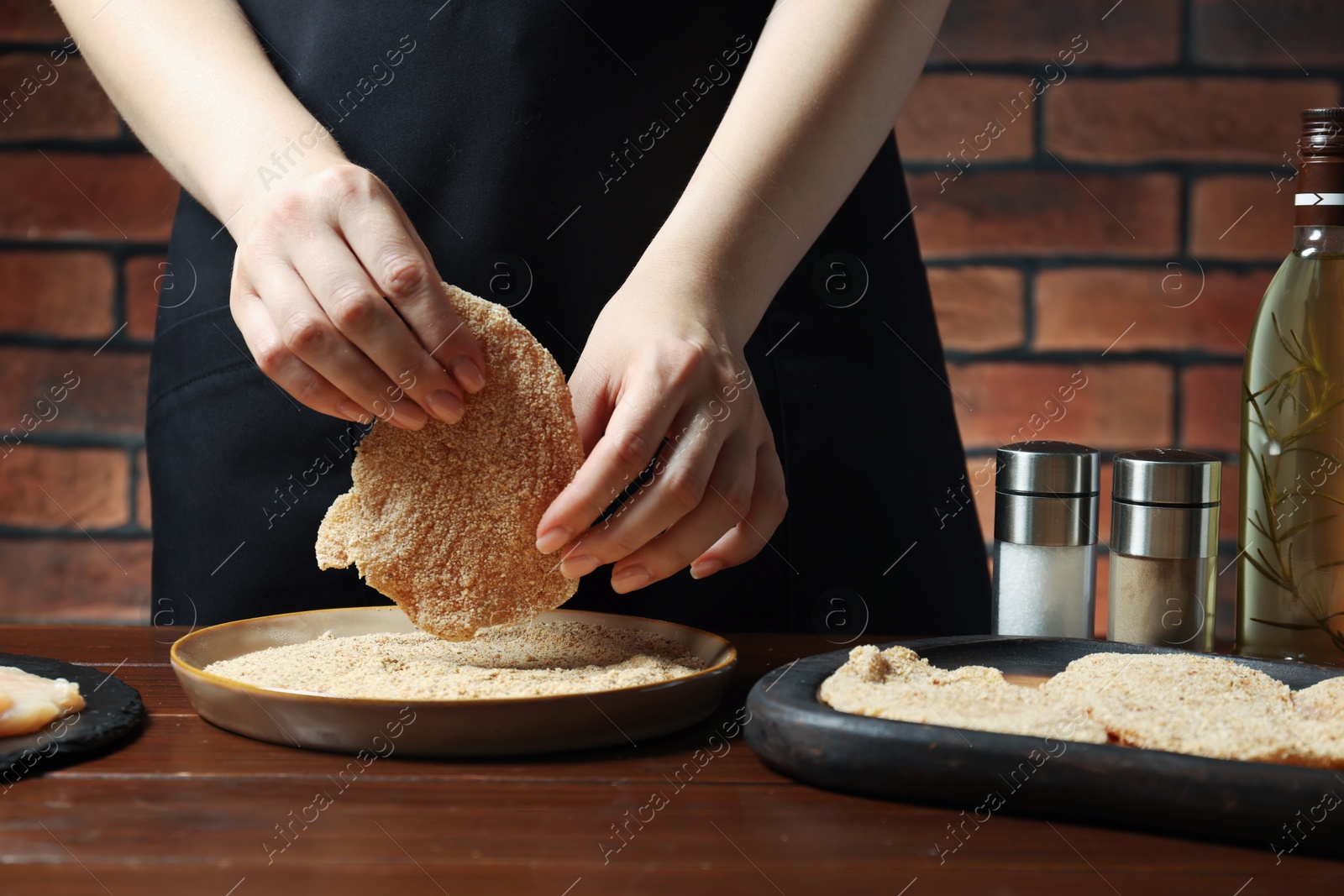 Photo of Woman making schnitzel at wooden table, closeup