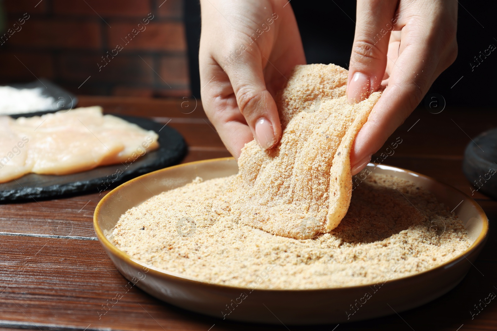 Photo of Woman making schnitzel at wooden table, closeup