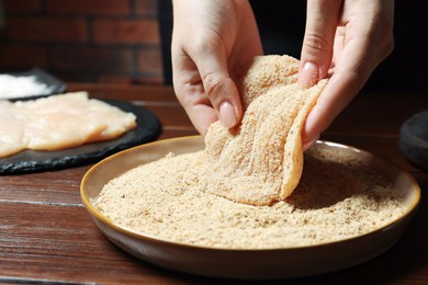 Woman making schnitzel at wooden table, closeup