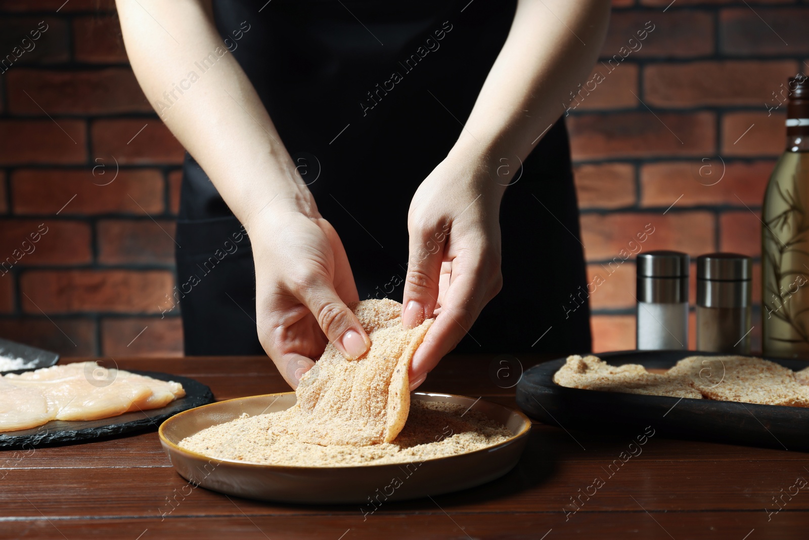 Photo of Woman making schnitzel at wooden table, closeup