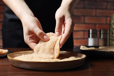 Woman making schnitzel at wooden table, closeup