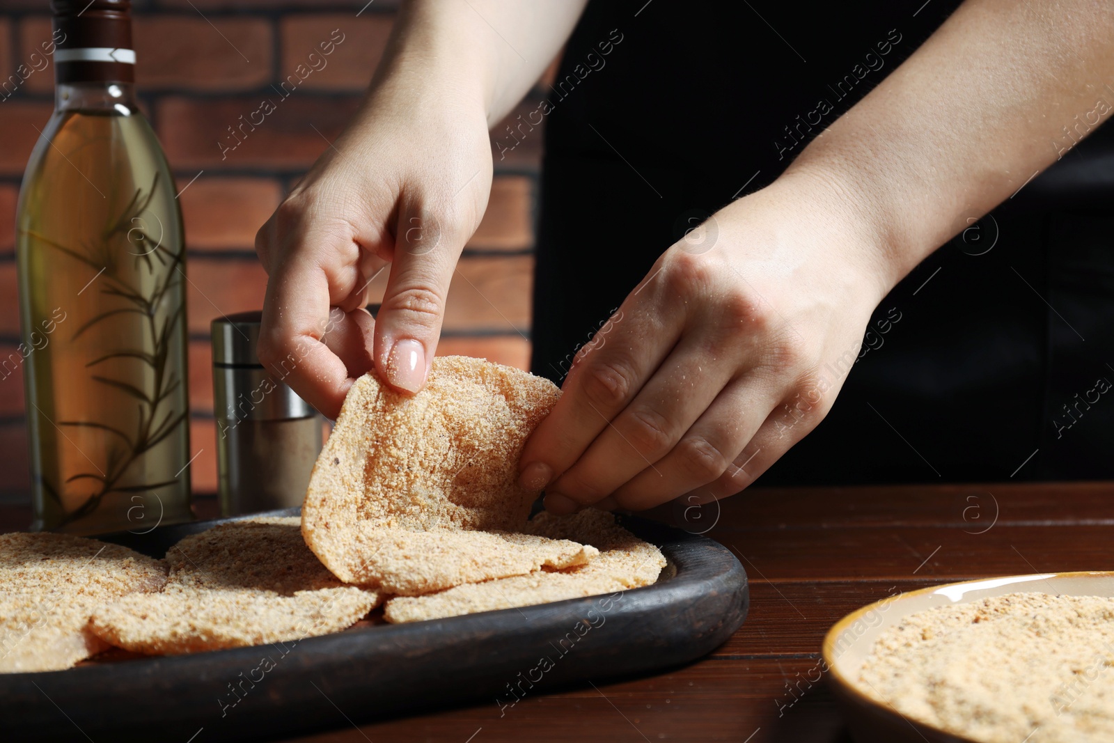 Photo of Woman making schnitzel at wooden table, closeup