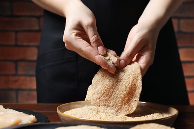 Woman making schnitzel at wooden table, closeup