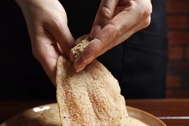 Woman making schnitzel at wooden table, closeup