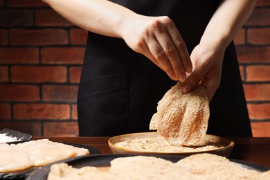 Photo of Woman making schnitzel at wooden table, closeup