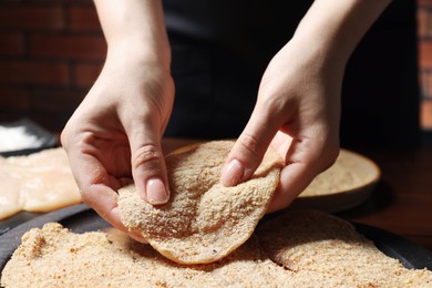 Woman making schnitzel at wooden table, closeup