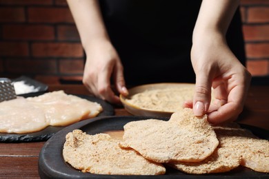 Photo of Woman making schnitzel at wooden table, closeup