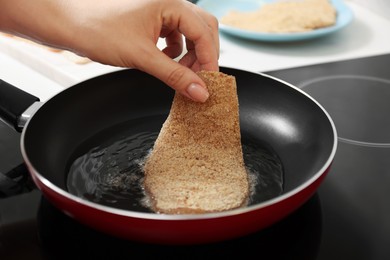 Photo of Woman cooking schnitzel in frying pan on stove, closeup