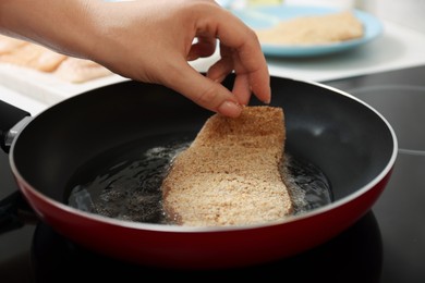 Photo of Woman cooking schnitzel in frying pan on stove, closeup