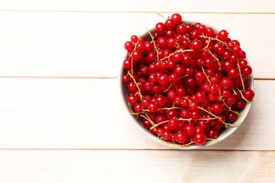 Photo of Fresh red currant berries in bowl on white wooden table, top view. Space for text