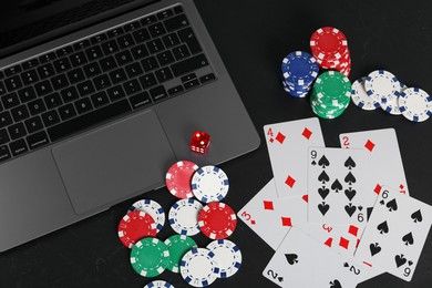 Photo of Online poker. Playing cards, chips, dice and laptop on black table, top view