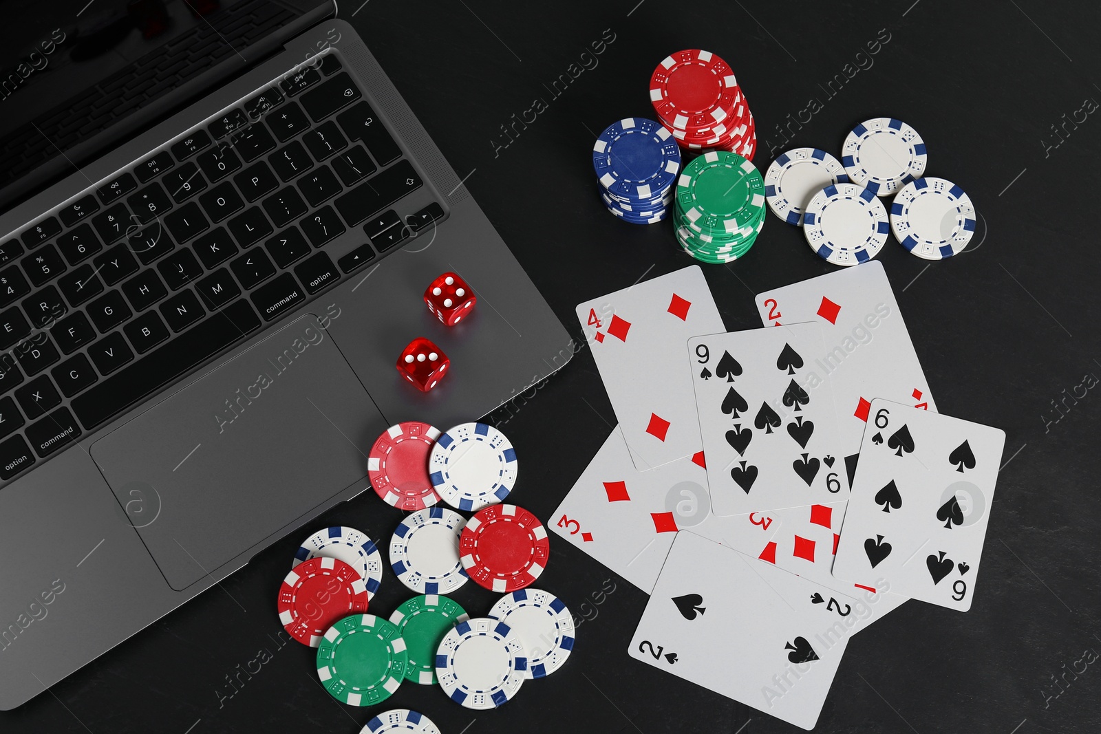 Photo of Online poker. Playing cards, chips, dice and laptop on black table, top view