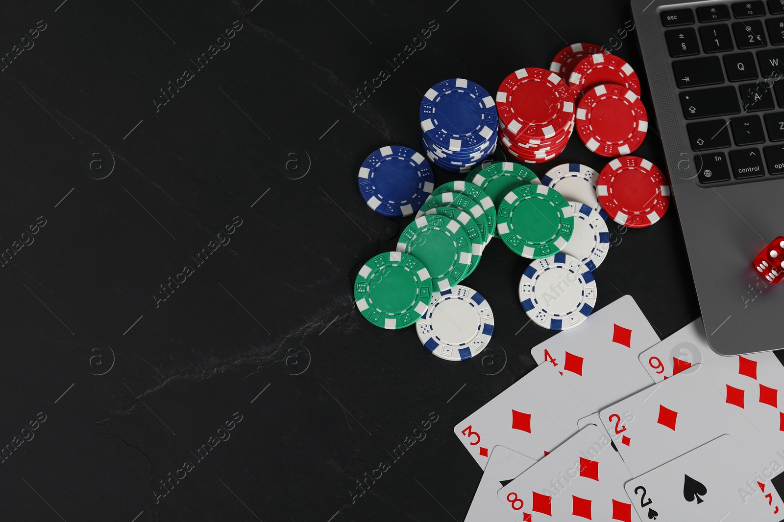 Photo of Online poker. Playing cards, chips, dice and laptop on black table, top view. Space for text